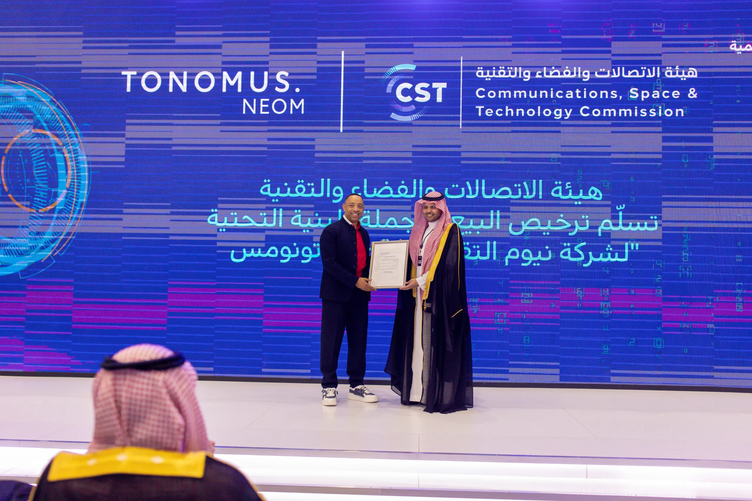 A certificate presented on stage between Tonomus and the Communications, Space & Technology Commission