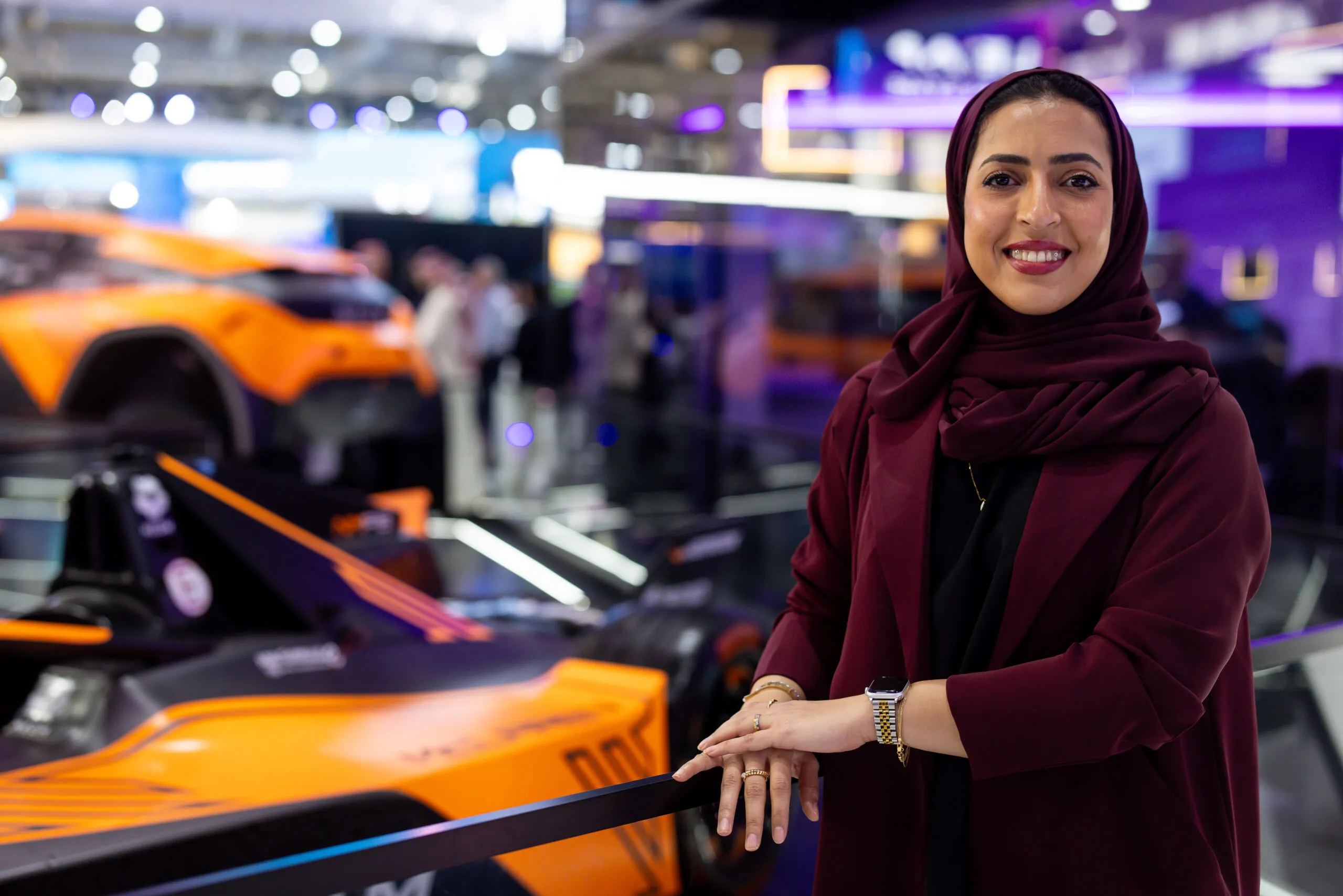 A woman posing beside the NEOM Formula E show car