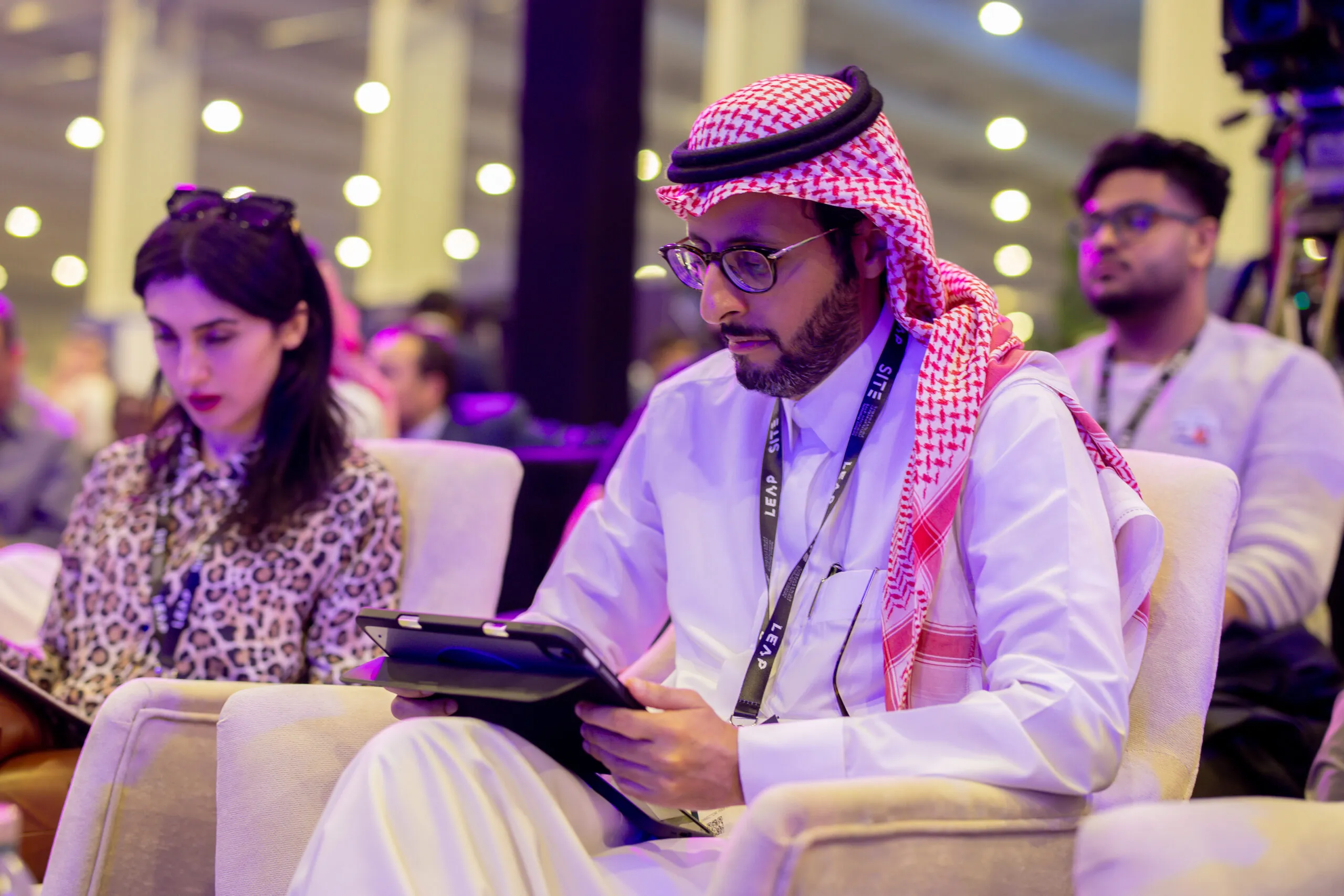 Delegates seated in the audience, one making notes on a tablet