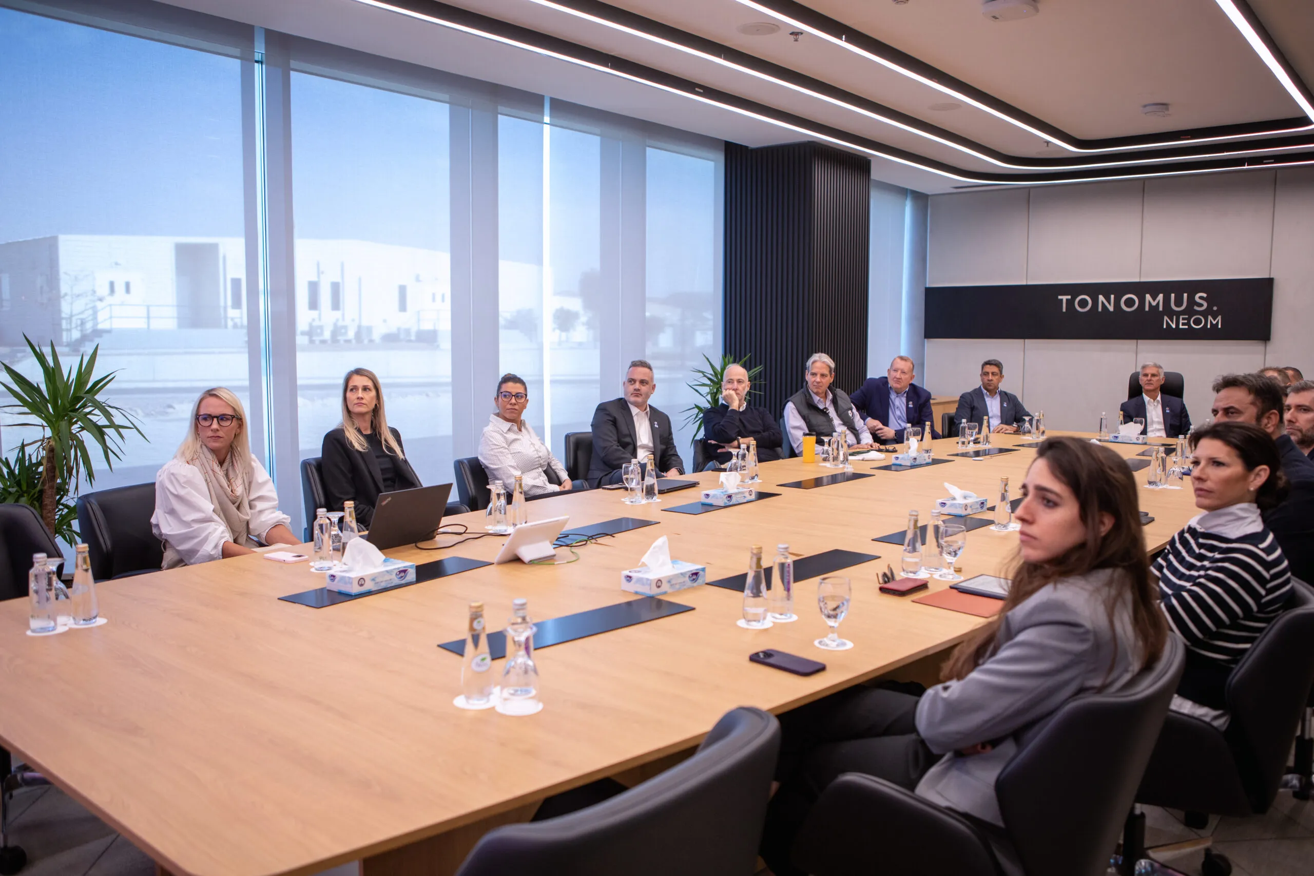 A meeting around a long boardroom table beneath the Tonomus NEOM sign