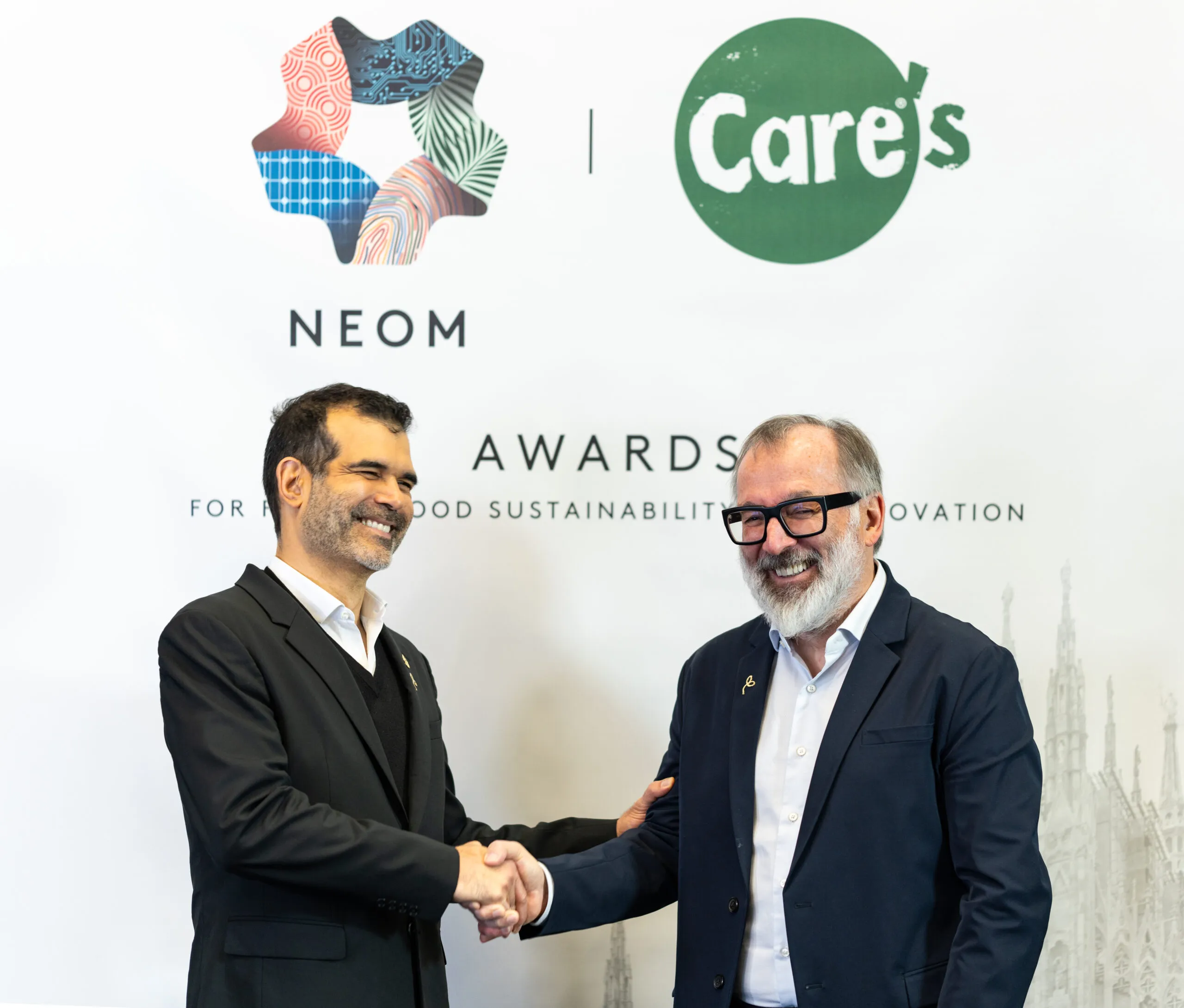Two men shaking hands beneath the NEOM and CARE's Awards backdrop