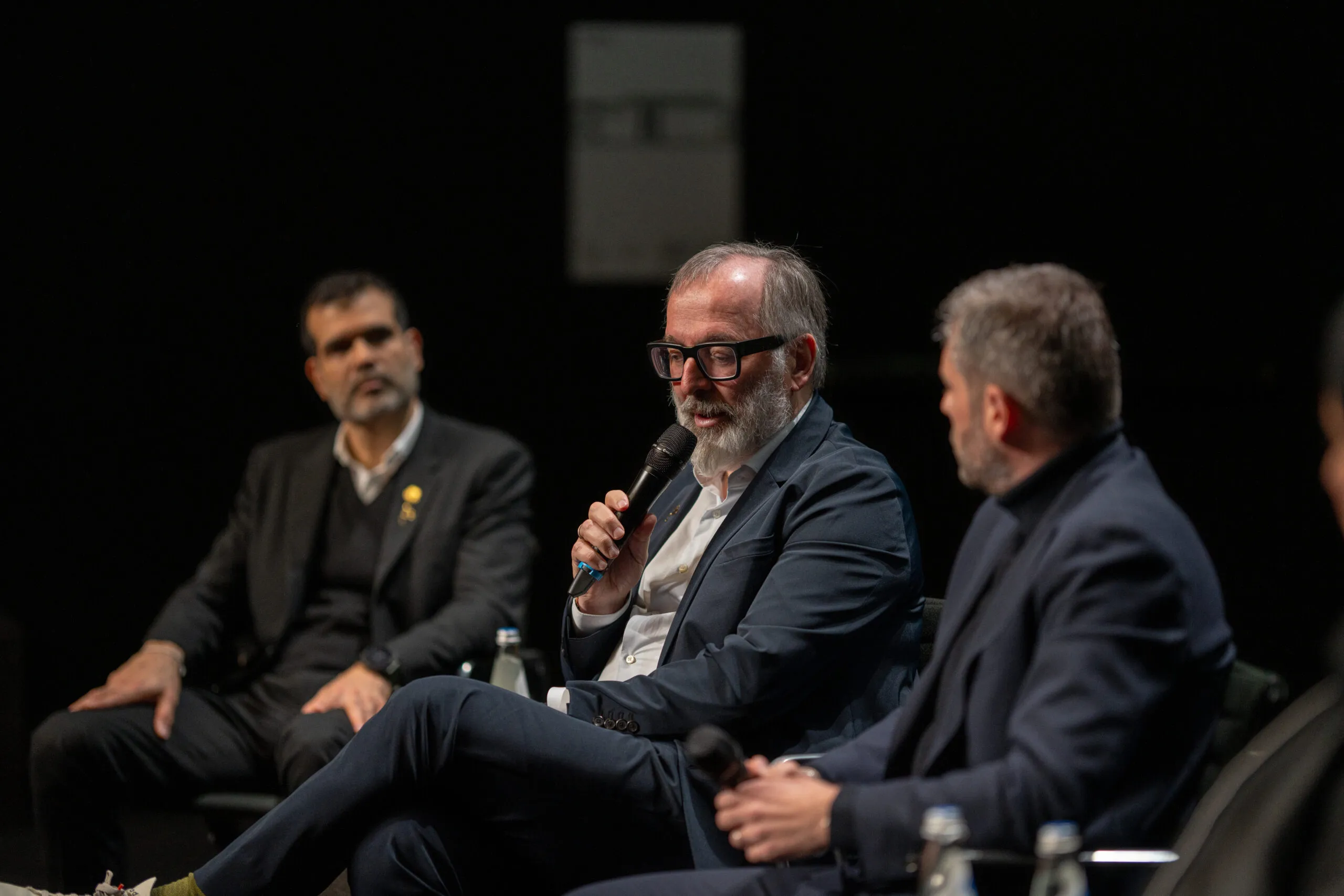 Three panellists in discussion, one speaking into a microphone