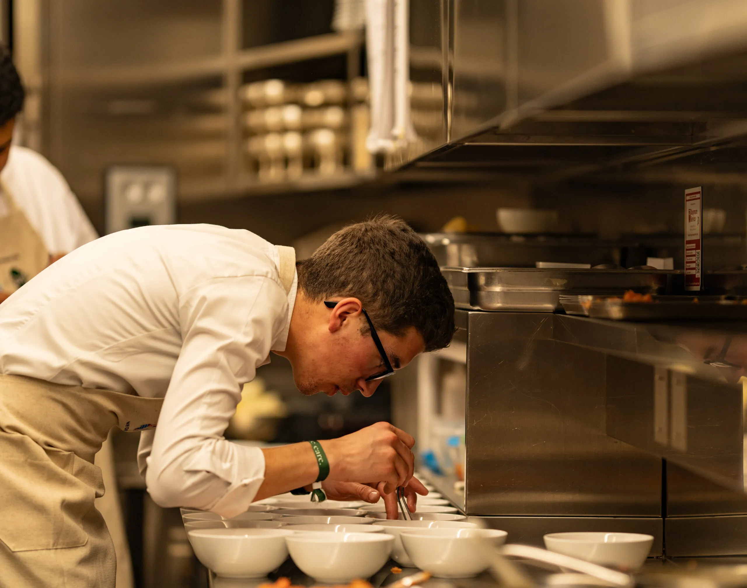 A chef leaning in to plate a course at the kitchen pass