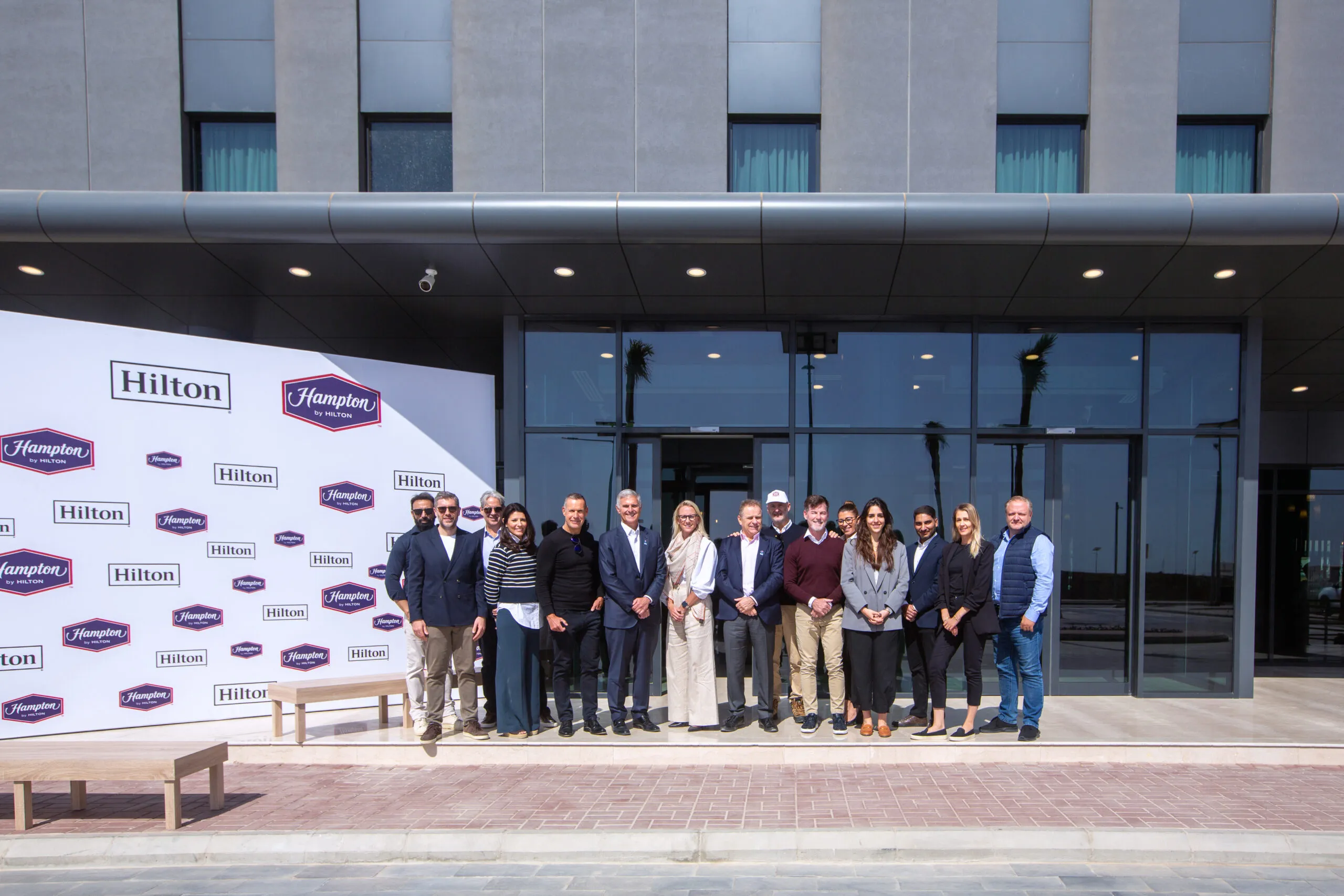 A group photograph before the Hilton and Hampton press wall outside the hotel