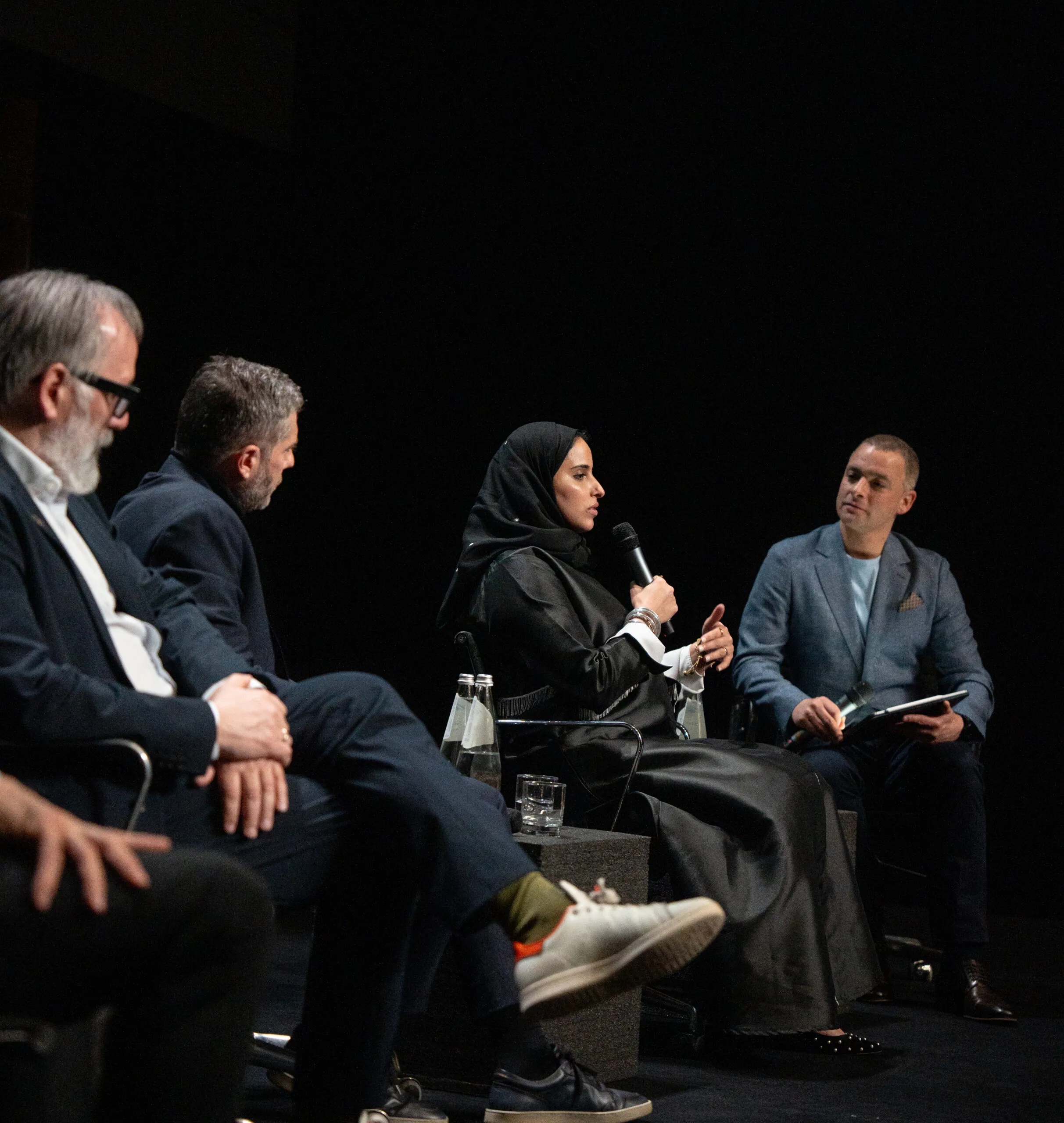 A woman speaking into a microphone during the panel, seated among the guests