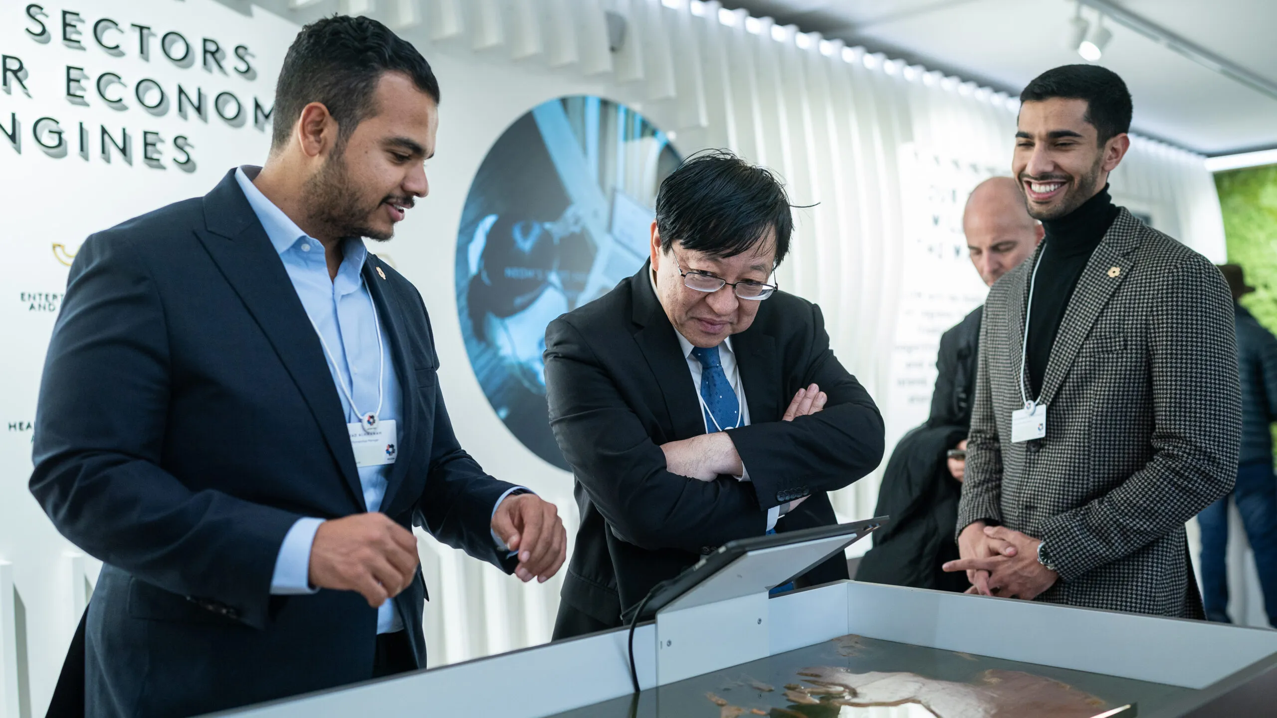 Visitors leaning in to study a tabletop exhibit, one with arms crossed