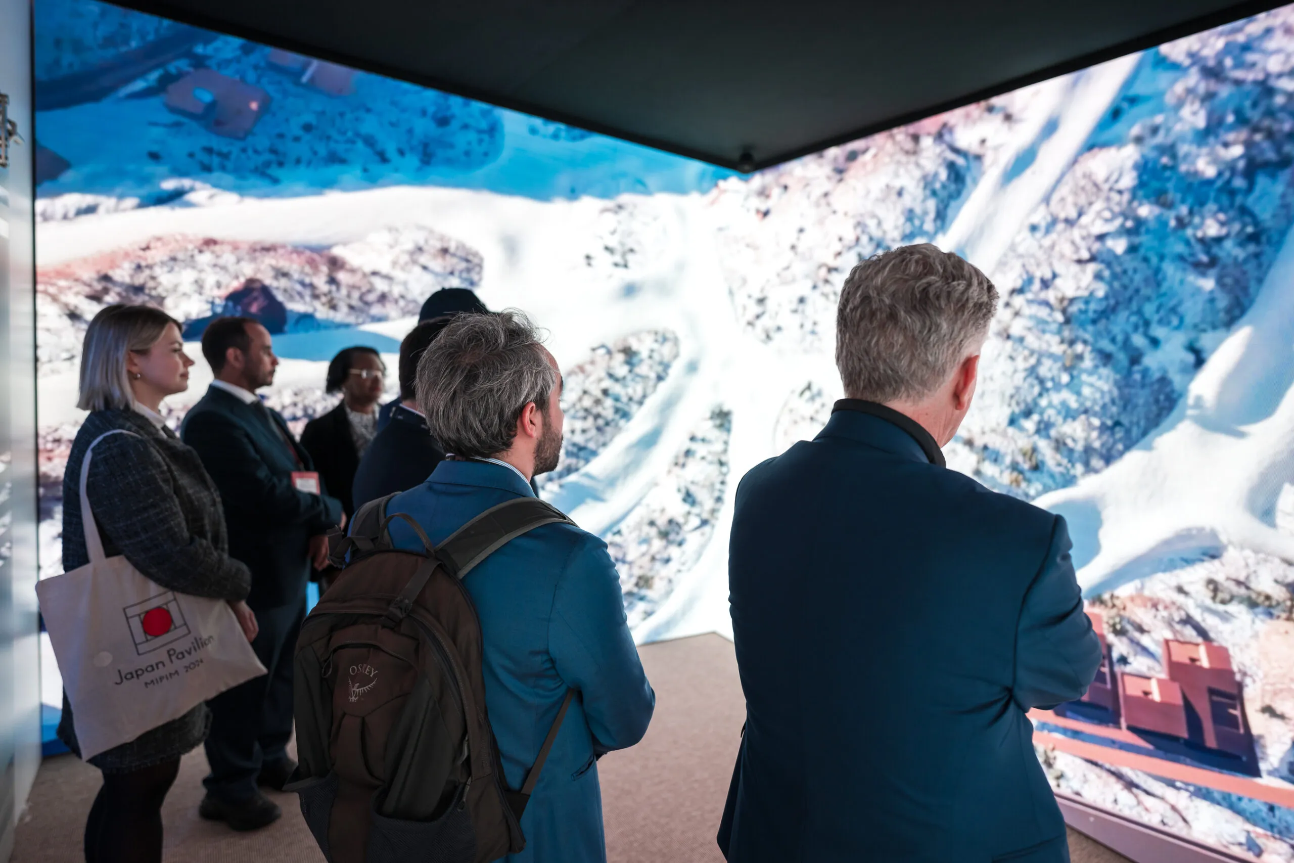 Visitors watching an aerial film of snow-dusted mountains on a wall-sized screen