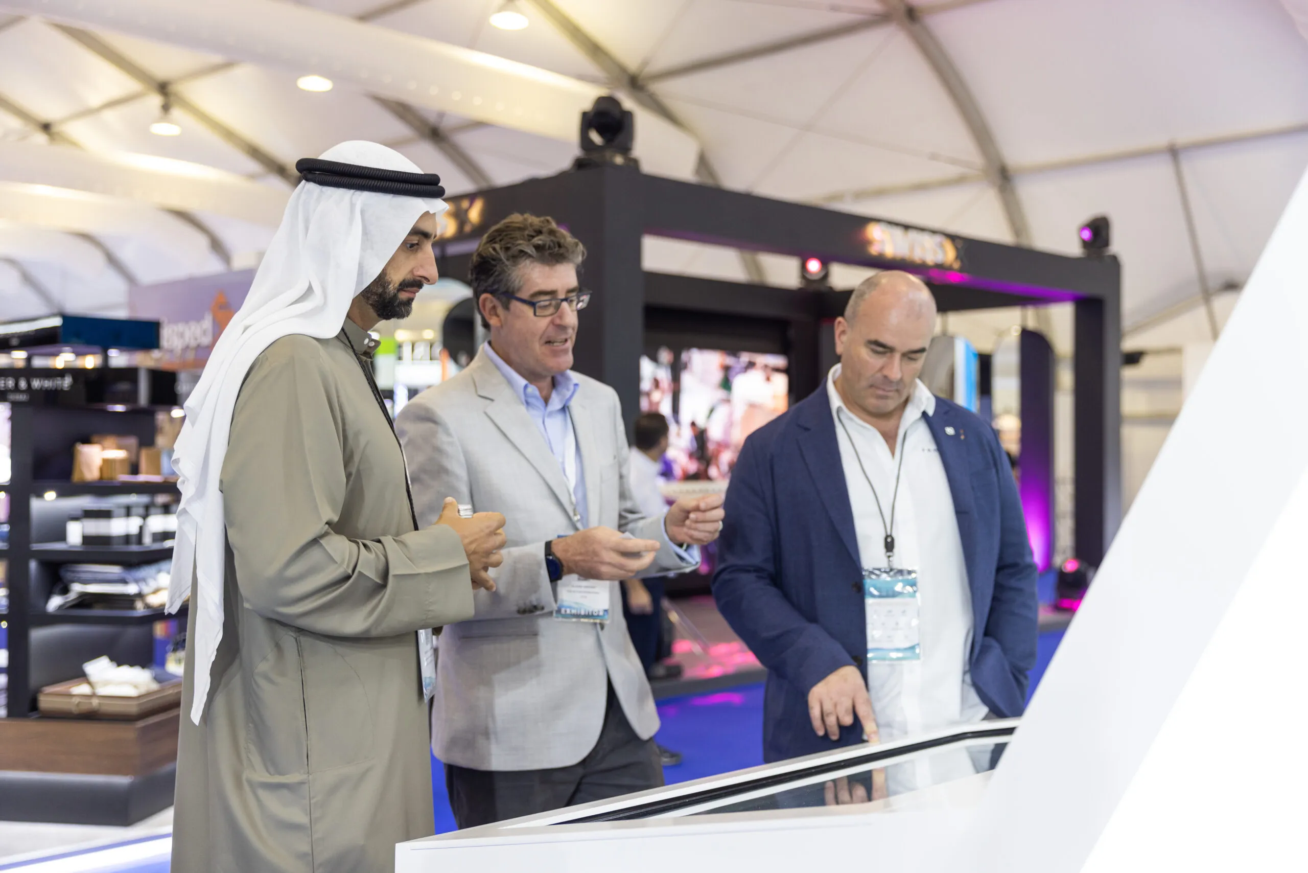 Three guests in conversation beside a display table, one in traditional Emirati dress