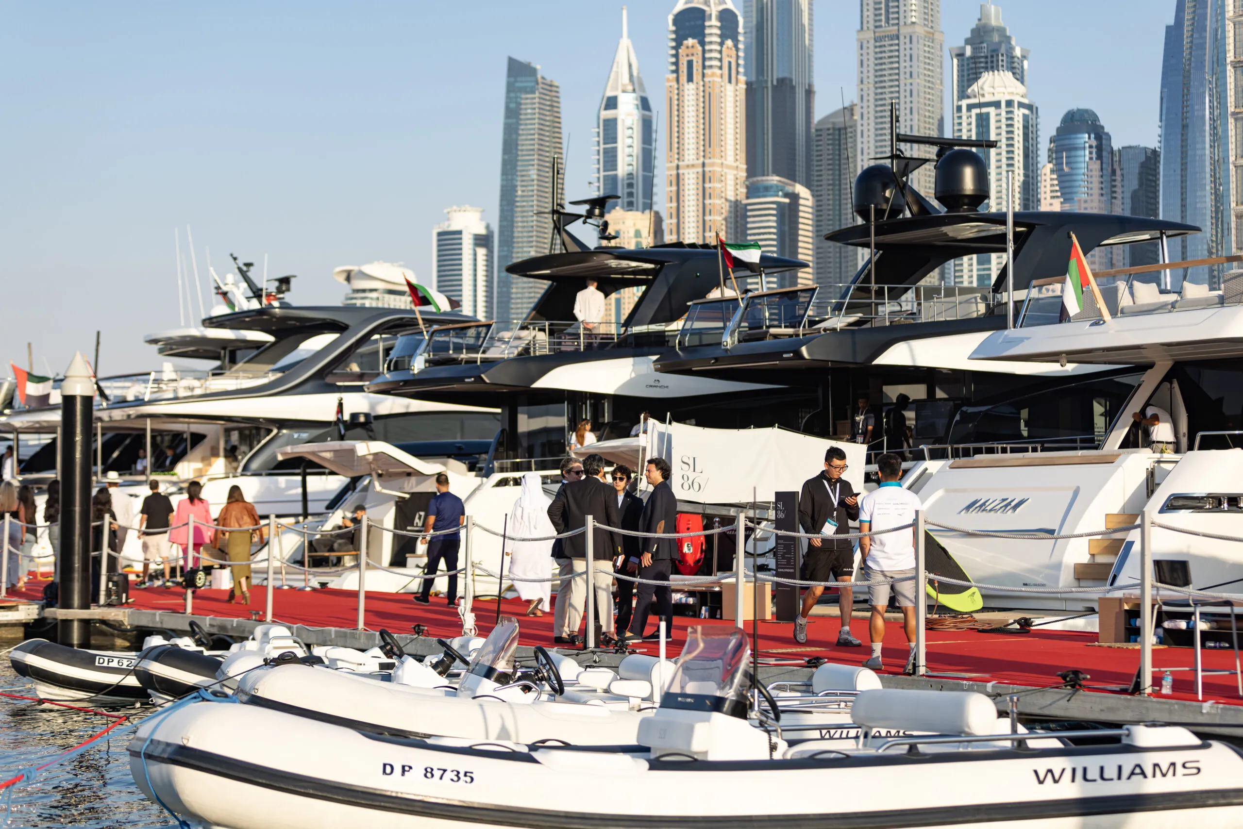 Motor yachts and tenders moored along a red-carpeted dock, with the Dubai Marina skyline behind