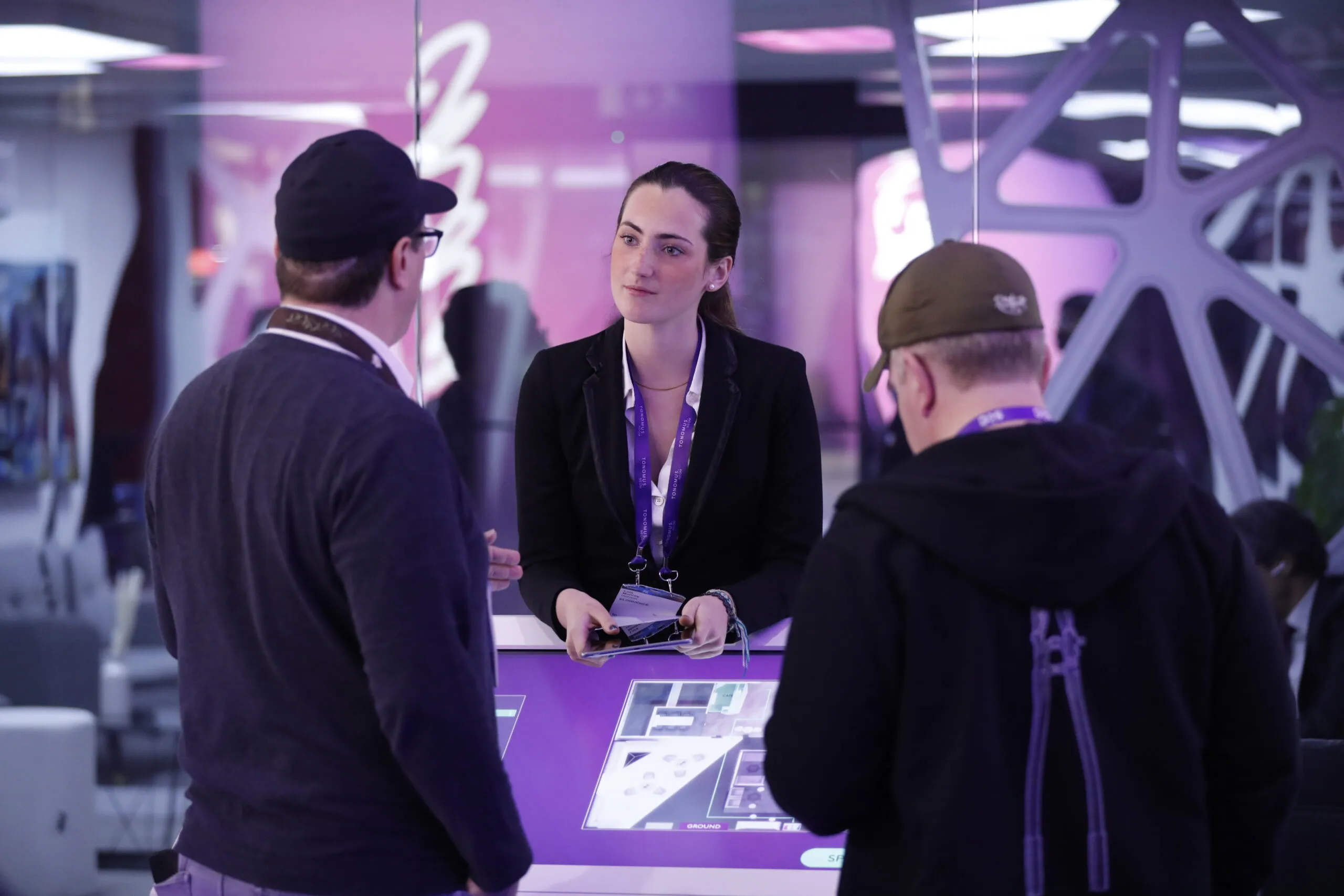 A host at a violet-lit touch table talking with two visitors