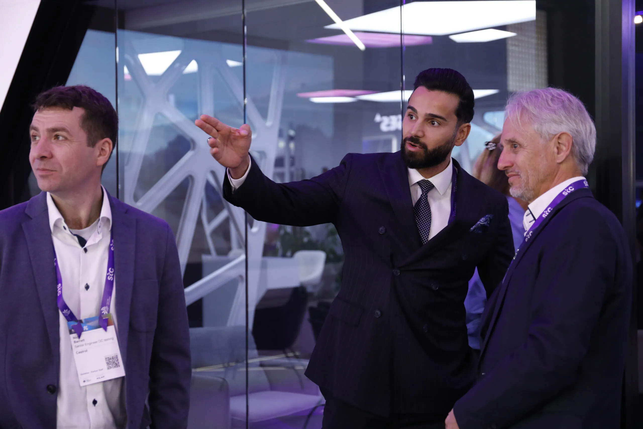 A guide gesturing towards the booth's glass wall as he shows guests around