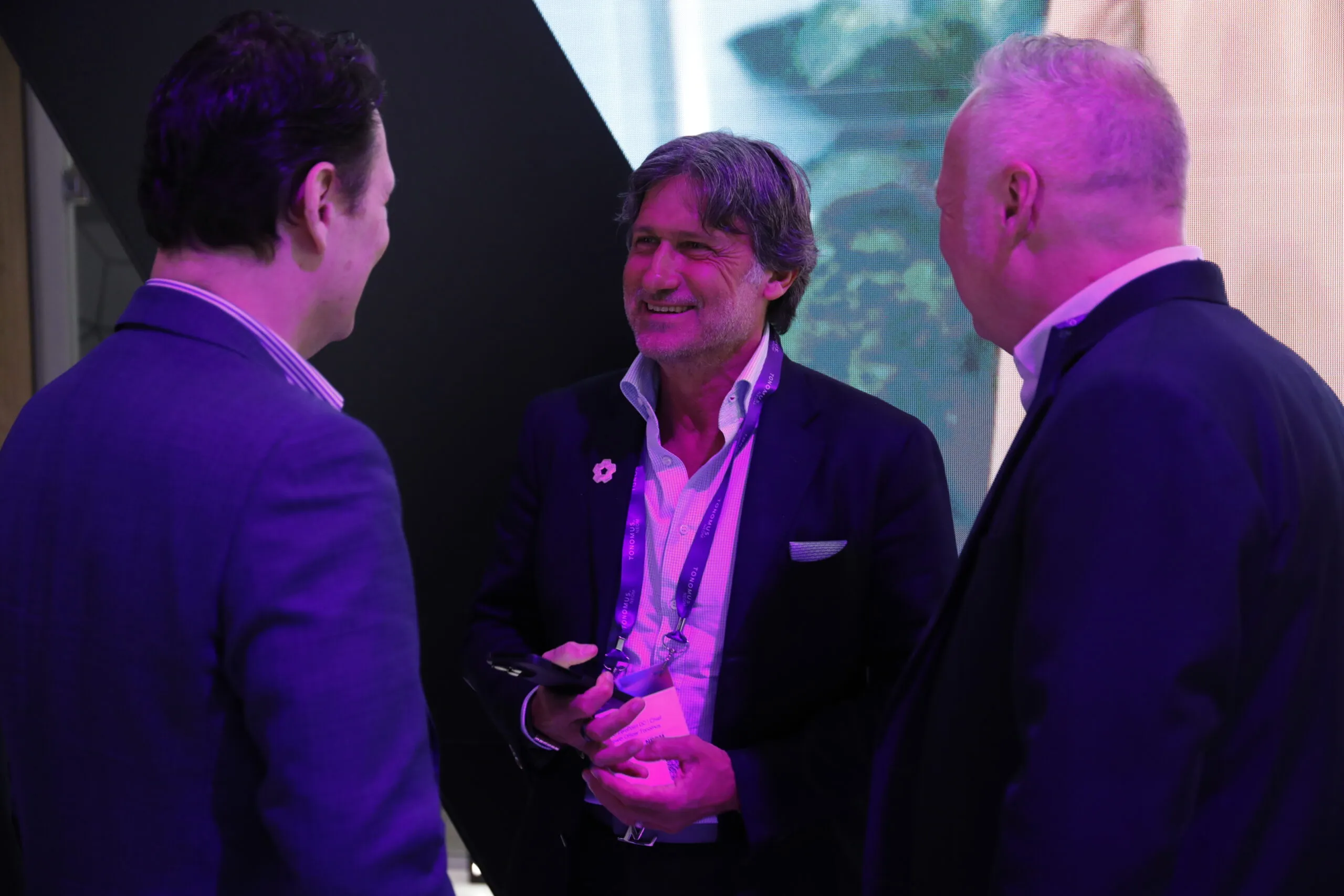 Three delegates in conversation under the booth's violet lighting