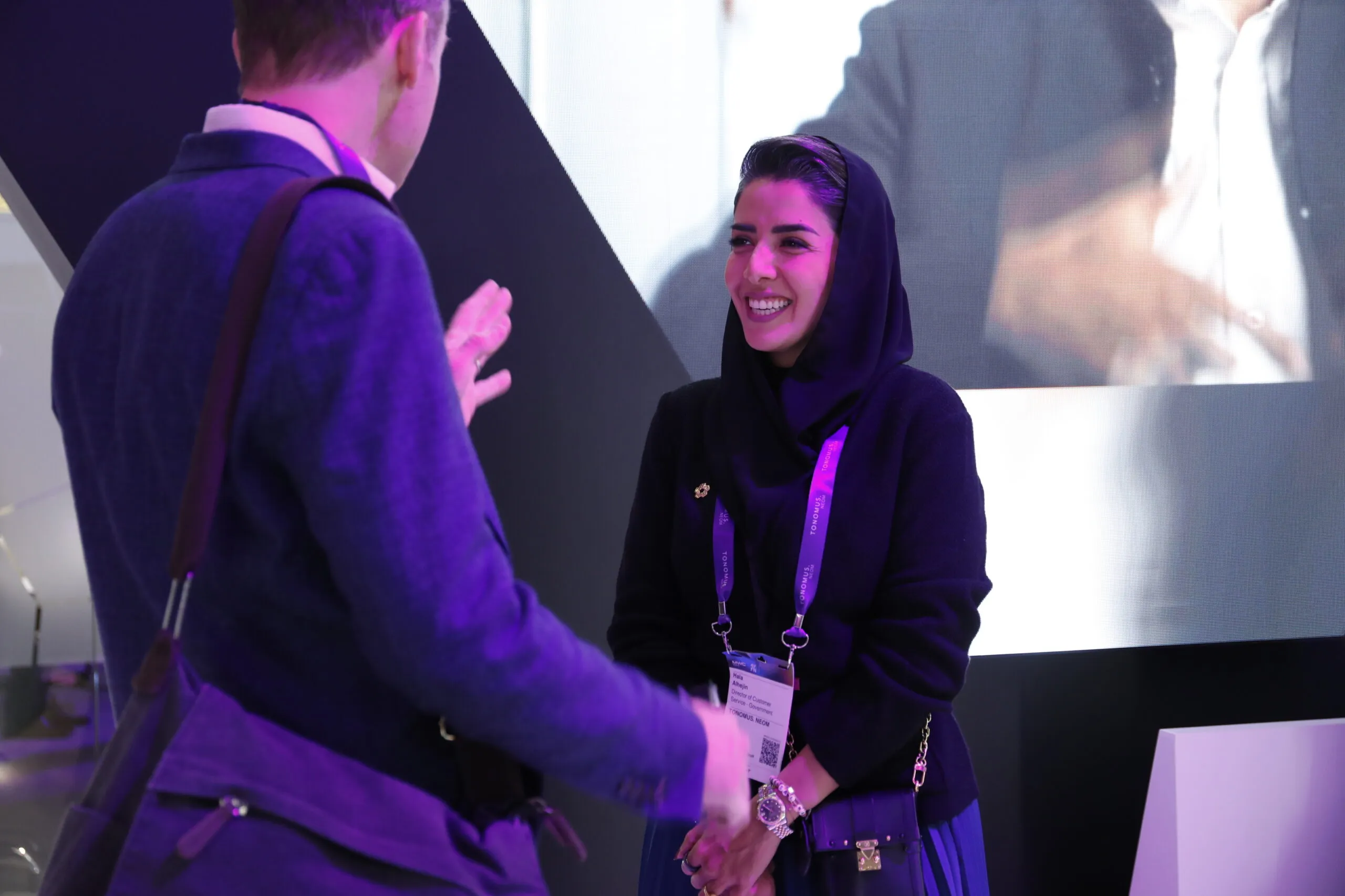 A smiling woman in a headscarf greeting a visitor with a handshake