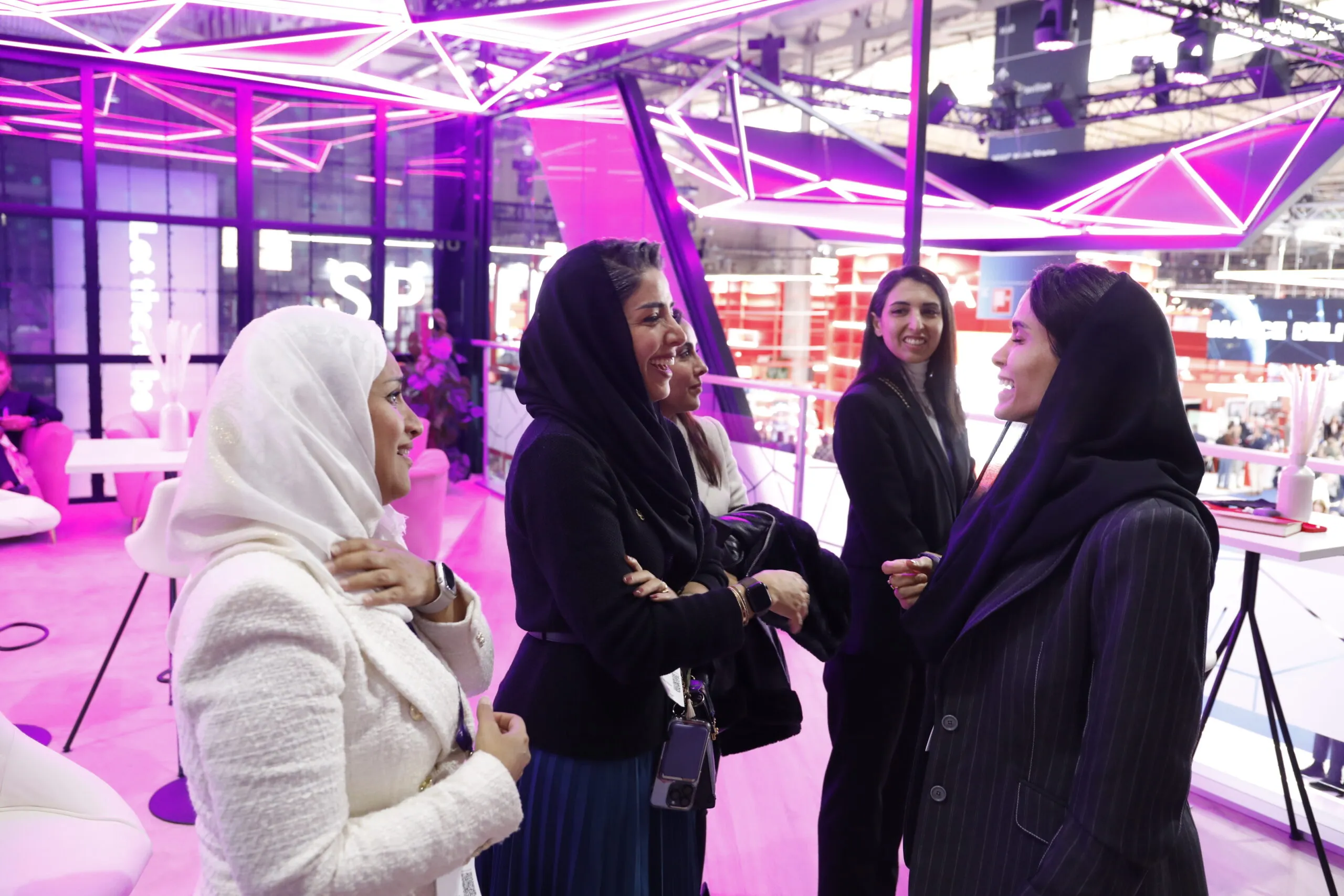A group of women in conversation beneath the booth's neon canopy