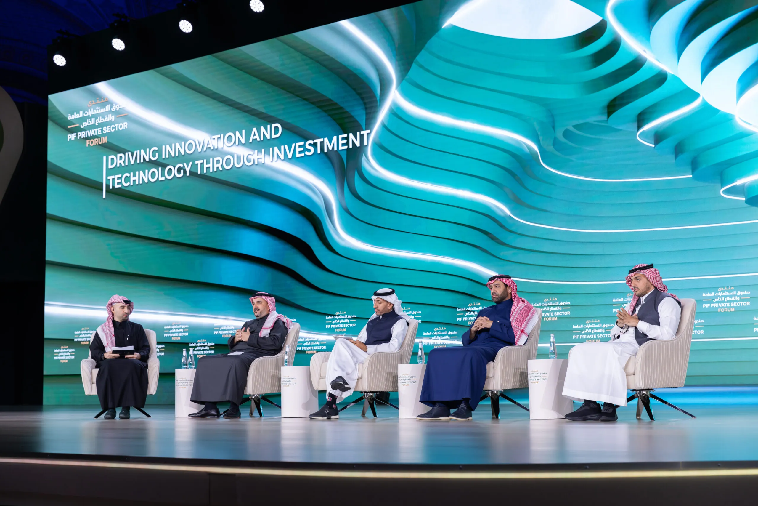 A panel discussion on stage, titled 'Driving innovation and technology through investment'