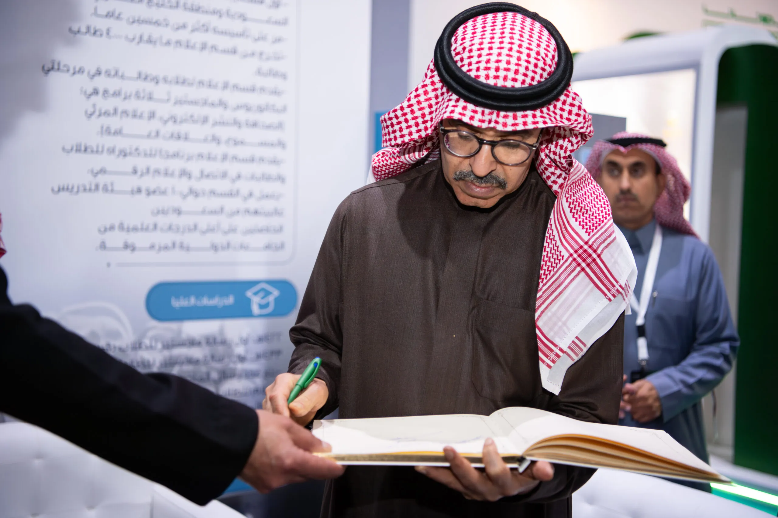 A guest in a red-checked shemagh signing the visitors’ book